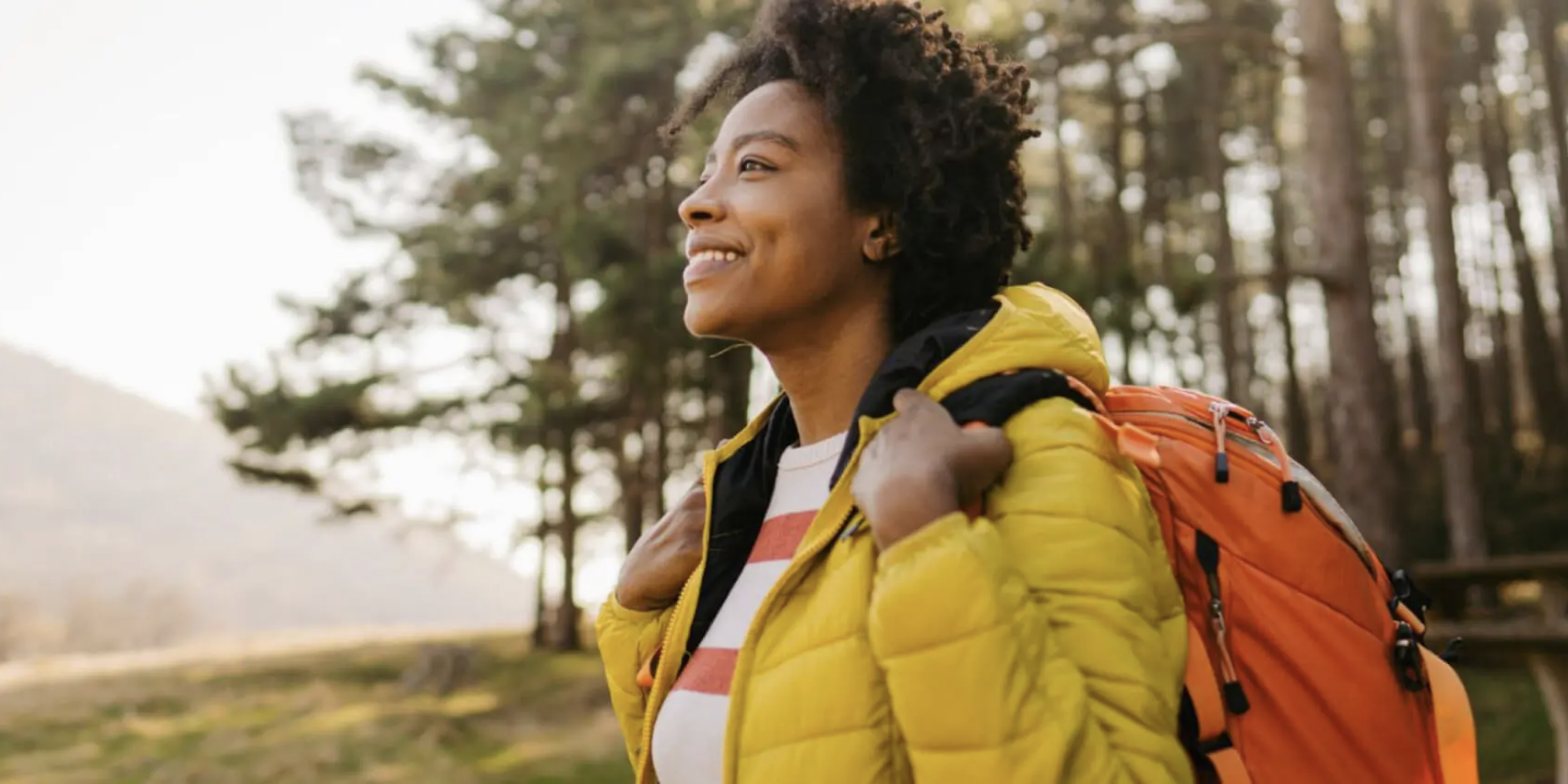 A woman outdoors with a backpack, smiling toward the sun